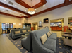 A modern hotel lobby with gray sofas, wooden tables, a TV on the wall, and contemporary lighting.