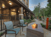 Patio with two chairs and a rectangular fire pit in front of a building, surrounded by landscaped greenery and stone pathways.
