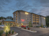 A four-story Hampton Inn hotel with a parking lot, surrounded by greenery, at dusk.