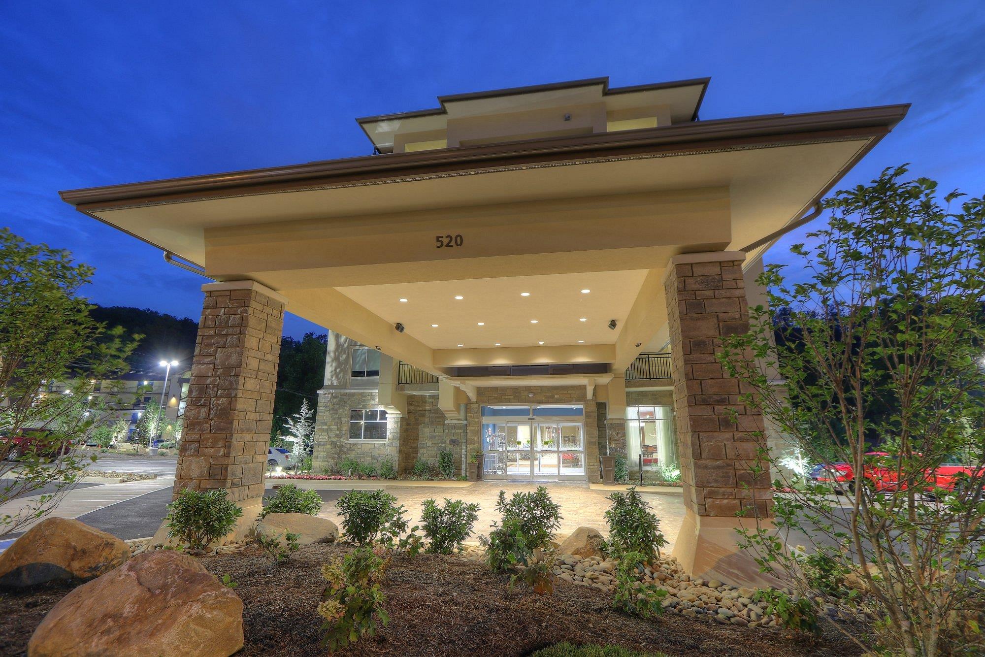 The image shows the entrance of a modern building with stone pillars, landscaped plants, and the number 520 above the doorway, taken at dusk with outdoor lights on.