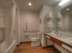 Accessible bathroom with walk-in shower, grab bars, toilet, sink with counter, stacked towels on shelves, large mirror, and wooden-style floor.
