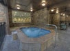 Indoor hot tub with bubbling water, surrounded by stone walls and tile, with metal handrail and seating area in the background.