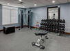 A fitness room with exercise equipment, including a weight bench, dumbbell rack, kettlebells, a cable machine, and an exercise box, with a mirror and window in the background.