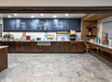 Breakfast buffet area with various hot and cold food options, drinks, and cereals displayed on a counter under a decorated wall.