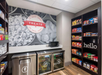Snack shop with shelves of chips and candy, a wall of drinks in coolers, and a microwave on the counter. Large wall mural with "TREATS" written on it.