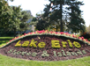 A flower bed with the text "Lake Erie Shores & Islands" composed of yellow and white flowers, surrounded by red flowers and trees in the background.
