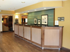 Hotel front desk area with wooden counter, green and beige walls, framed art, and a sign indicating "Manager on Duty.