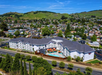Aerial view of a large hotel with a pool, surrounded by residential houses and greenery under a clear blue sky.