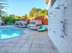 Poolside area with a tiled shower wall, three cabanas with turquoise cushions, and a clear blue swimming pool, surrounded by greenery and wooden fencing.