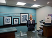 Hotel reception area with a staff member standing behind the desk. Walls display black and white photos. A sign reads "Hilton HHonors.
