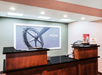 Hotel reception desk with a large framed artwork behind, featuring a ferris wheel and the word "enjoy." There are brochures and a phone on the counter.