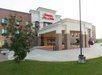 Exterior view of Hampton Inn & Suites hotel with a covered entrance, surrounded by grass and a few trees.