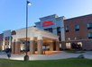 Exterior view of a Hampton Inn & Suites hotel with a modern entrance, three-story building, and parking lot in front.