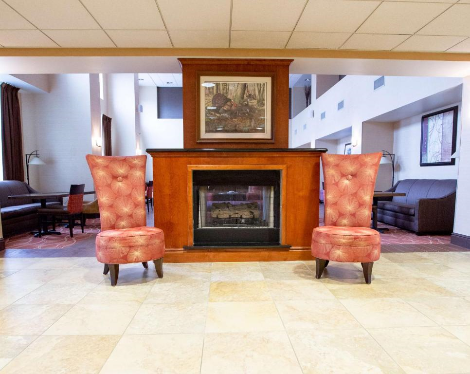 A hotel lobby with a fireplace framed by two tall red chairs, a painting above, and dark seating areas in the background.