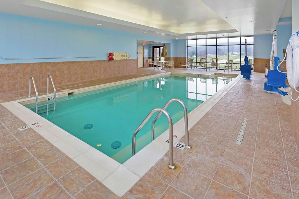 Indoor swimming pool with light blue water and tiled floor. There are metal ladders on both sides and large windows in the background.