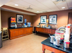 A hotel breakfast area with a beverage dispenser, cereal containers, and food trays on wooden counters under framed pictures.