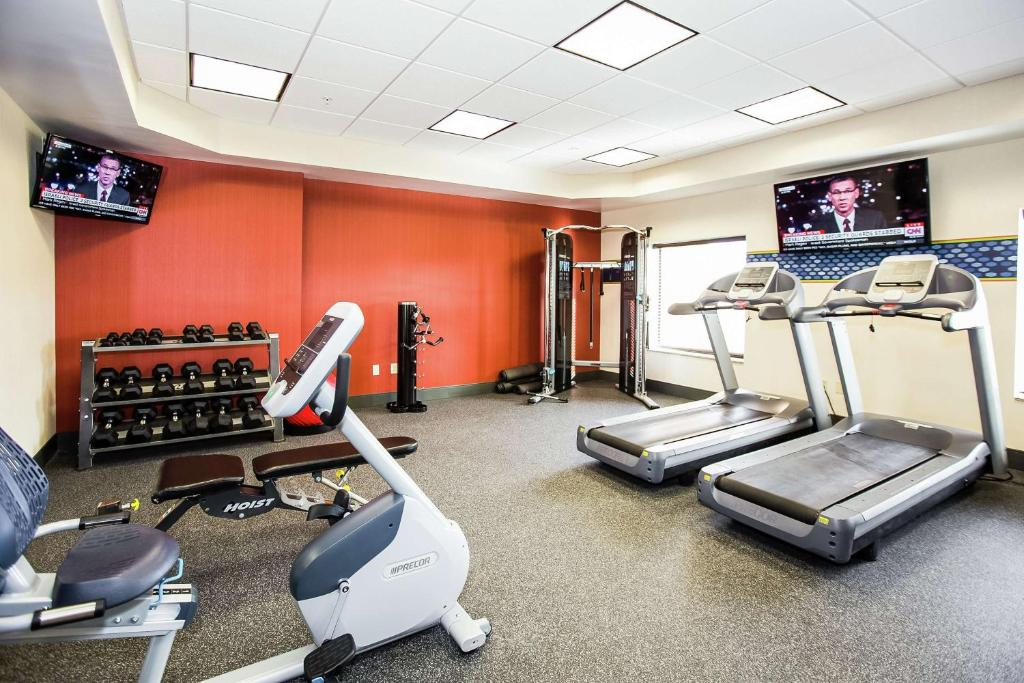 A gym with two treadmills, an exercise bike, a cable machine, various weights, and two TVs on red and white walls.
