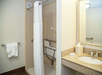 Accessible bathroom with a walk-in shower, grab bars, a white shower curtain, a towel on the rail, and a sink with a soap dispenser and tissue box on the countertop.