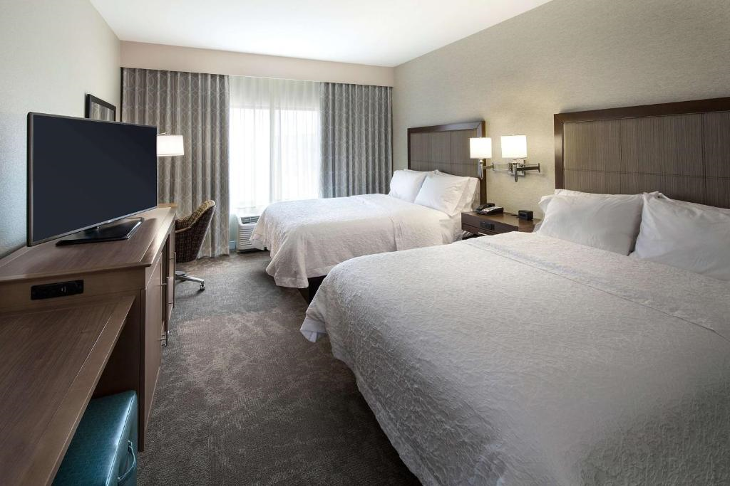 2 Queen beds, work area, and a flat-screen TV inside a guest room.
