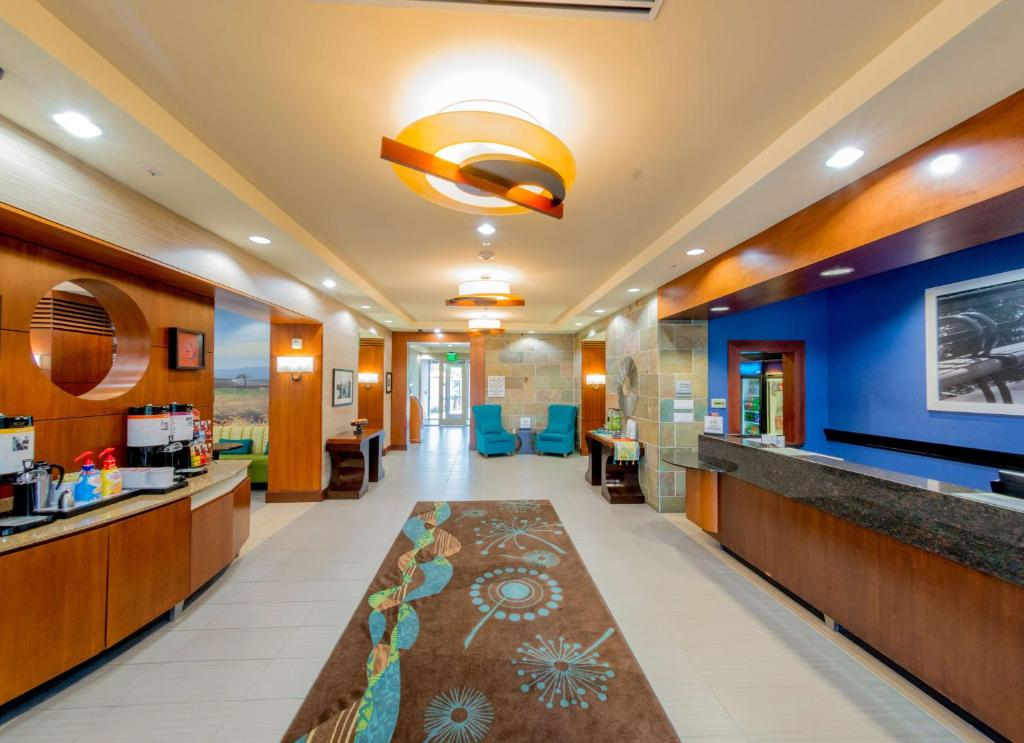 A hotel lobby with modern decor, featuring a long patterned rug, reception desk, seating area, and vibrant lighting fixtures.