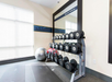 A gym corner with a rack of dumbbells, exercise mats on the floor, and a large mirror on the wall.