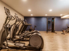 A modern gym with exercise equipment, including ellipticals, a treadmill, a stationary bike, and a strength training machine, on a wooden floor with overhead lighting.