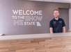 A person standing behind a wooden reception desk under a sign reading "Welcome to the Show Me State" with a silhouette of Missouri.