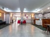 Hotel lobby with tiled floors, two red chairs in the center, a wooden reception desk on the right, and wall art behind the seating area.