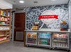 Small self-serve snack area with shelves of chips and candy, refrigerated drinks, and a sign reading "TREATS" on a wall with popcorn and pretzel graphics.