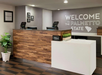 Hotel reception area with a wooden desk, potted plant, and a sign reading "Welcome to the Palmetto State." Two card payment machines are visible on the counter.