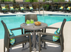 Poolside table with wicker chairs, a tray of green drinks, and a bowl of cookies. Lounge chairs with striped pillows are in the background by the pool.
