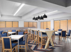 A modern dining area with blue chairs, white tables, high-top seating, wooden blinds, and pendant lights in a bright, spacious room.