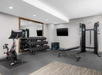 Modern gym with a stationary bike, dumbbell rack, weight bench, cable machine, two wall-mounted TVs, large mirror, and gray flooring.