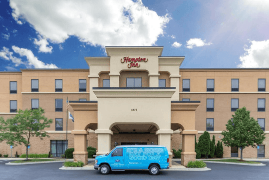 The front exterior of the Hampton Inn with a bright blue van parked out front in Minneapolis, Minnesota.