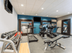 A small gym with several different types of equipment, a blue accent wall, and several mirrors around the room.