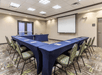 A meeting room with three blue cloth covered tables set up in a "U" with a projector on the front wall.