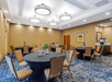 A conference room with round tables covered in black cloth, surrounded by beige chairs. The room is well-lit with modern ceiling lights and has a carpeted floor with a blue and beige pattern.