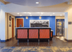 Hotel lobby with a reception desk featuring red paneling, a mountain photo on the wall, and a small adjacent shop with a fridge.