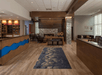 Hotel lobby with wooden flooring, a blue patterned rug, and modern decor. Seating area with a fireplace is visible, along with a reception desk on the left.