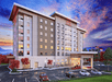 The front exterior of the Hampton Inn & Suites Asheville Biltmore Area with cars parked in the lot in front of it and a purple sunset behind it.