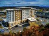 Aerial view looking down on the front exterior of the Hampton Inn & Suites Asheville Biltmore Area with fall trees in front and mountains in the background.