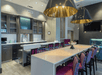 A modern dining area with a long hightop table with purple chairs and a bar on the far left wall in the lobby of the Hampton Inn & Suites Asheville Biltmore Area.