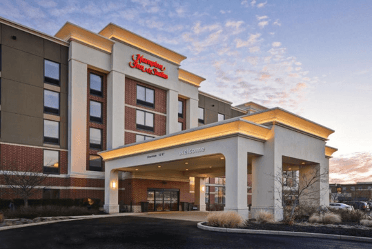 The front exterior of the Hampton Inn & Suites Columbus-Easton Area at sunset with scattered clouds in the sky.