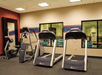 A small fitness center with two treadmills, an elliptical, and a stationary bike in front of windows that show in an indoor pool.