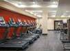 A fitness center with a row of cardio equipment in front of a red wall on the left side and a weights area with several machines on the right.