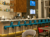 A silver bar with a row of turquoise chairs and other seating in front of it and a wall of the different alcohol they offer behind it.