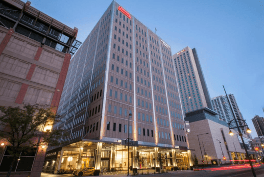 Street view of the Hampton Inn & Suites Denver Downtown Convention Center  at dusk with the lobby lights shining through the bottom floor windows.