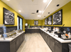 A hotel breakfast buffet area with food stations on both sides, black cabinets, yellow-green walls, and framed black-and-white photos on the walls.