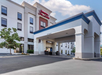 The image shows the exterior entrance of a Hampton Inn & Suites hotel with a covered driveway and clear sky above.