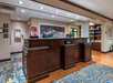 Hotel lobby front desk with dark wood finish, a patterned carpet, and a small shop area on the right. Overhead lighting illuminates the space.